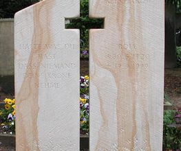 Gräber mit zwei großen, stilisierten Steinen und bunten Blumen davor auf einem Friedhof.