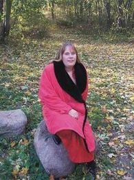 Eine Frau in einem roten Mantel sitzt im herbstlichen Wald auf einem großen Stein.