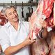 Butcher inspecting hanging meat in a shop.