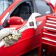Gloved hand holding a wrench near a red car with a toolbox in the background.