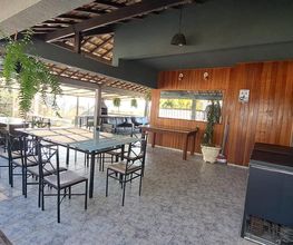 Área externa coberta com mesa e cadeiras, plantas suspensas e decoração em madeira.