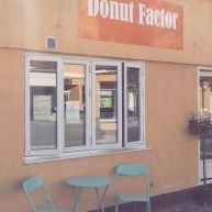 Facade af donutbutik med skilt, to blå stole og et bord udenfor.