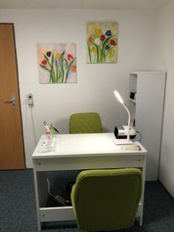 Büro mit grünem Stuhl, weißem Schreibtisch, Lampe und zwei Blumenbildern an der Wand.