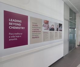 Corredor com cartazes sobre cultura corporativa e valores; mensagem: "Leading Beyond Chemistry".