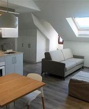 Sala de estar moderna con cocina integrada y sofá bajo ventana tipo tragaluz.