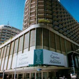 Edifício alto com placas indicando "Shopping Cassino Atlântico" sob céu azul.