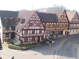 Fachwerkhäuser mit Ladenfront in einer Dorfstraße, umgeben von Pflastersteinen und ruhiger Umgebung.