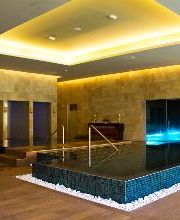 Piscina iluminada en un spa moderno con paredes de piedra y suelo de madera.