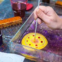 Hand creating marbling art with tool in tray of colorful ink and water.