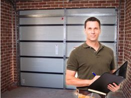 Man with a clipboard standing in a garage with brick walls and a metal garage door.