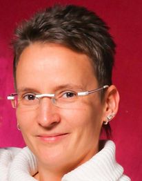 Eine Person mit Brille und kurzem Haar vor einem roten Hintergrund lächelt leicht.