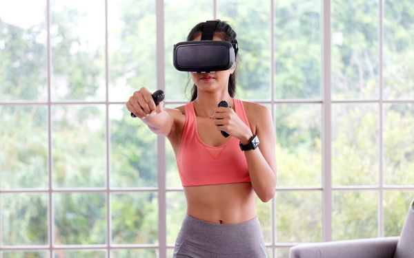 Eine Frau die mit einer VR Brille Boxübungen in ihrem Wohnzimmer macht.