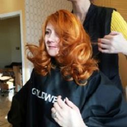 Woman with curly red hair styled at a salon, wearing a black cape.