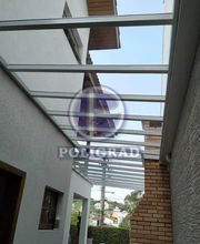 Cobertura de vidro entre edificações com paredes brancas e tijolos expostos.