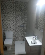 Baño moderno con ducha, lavabo y retrete. Pared con azulejos grises y marrones. Luz brillante.