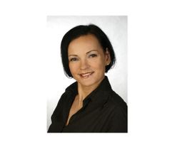 Eine Frau mit dunklem Haar trägt ein schwarzes Hemd und lächelt in die Kamera.