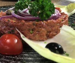 Rindertatar mit Petersilie, Zwiebeln, Tomaten und Oliven, auf einem Salatblatt serviert.