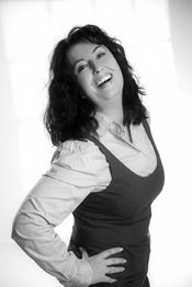 Eine Frau lächelt und posiert in Schwarz-Weiß mit einem Hemd und einer Weste.