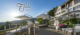 Frau im Bademantel auf Terrasse mit Sonnenschirmen, Blick auf Berge, Thula Wellnesshotel-Logo.