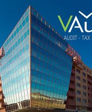 Edificio moderno con fachada de vidrio, logo de VAudit y lista de servicios en esquina superior derecha.