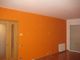 Habitación con pared naranja, puerta de madera y ventana cerrada con persiana bajada.