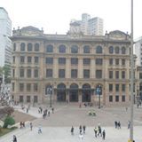 Prédio histórico em praça movimentada com pessoas caminhando ao redor.