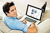 Homem sorrindo sentado no sofá com laptop no colo, navegando na internet.