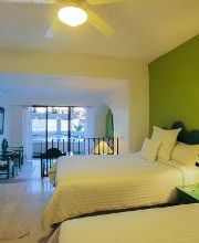 Habitación doble, paredes verde y blanca, dos camas, lámpara de mesa y balcón al fondo.