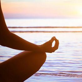 Persona meditando en la playa al atardecer frente al mar.