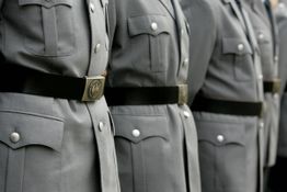 Reihe von Personen in grauen Militäruniformen. Fokus liegt auf den Gürtelschnallen und Knöpfen.