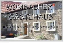 Stein-Gästehaus mit Schriftzug "Wombachers Gästehaus - Genussvoll entspannen" auf rotem Dach.