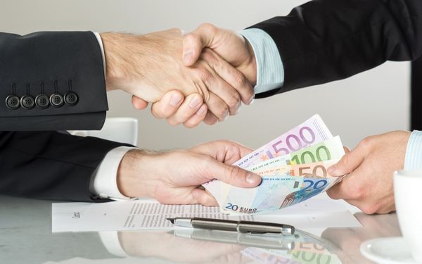 Geschäftsleute besiegeln eine finanzielle Vereinbarung per Handschlag, während Euro-Banknoten übergeben werden.