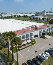 Edificio industrial con estacionamiento lleno, rodeado de áreas verdes y otras instalaciones.