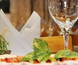Pizza mit Basilikum, Weingläsern und Servietten in einem Restauranttisch-Arrangement.