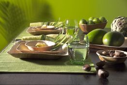 Grüner Tisch mit Geschirr, Artischocke, Avocados, Limetten und Nüssen in natürlicher Dekoration.