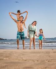 Familia feliz caminando en la playa, el padre lleva a un niño sobre los hombros.
