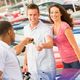Couple receiving car keys from a salesman at a car dealership, surrounded by parked cars.