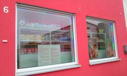 Rotes Gebäude mit zwei Schaufenstern, das Lebensmittel und südasiatische Produkte zeigt.