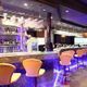 A modern bar with high stools and purple lighting creates a welcoming atmosphere.