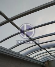 Teto curvo de vidro com estrutura metálica, sob céu nublado.