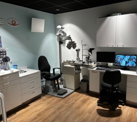 Optometriekamer met oogmeetapparatuur, bureau, stoelen, computer en opslagkasten.