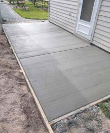 Freshly poured concrete patio next to a house with a white door and green lawn.