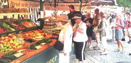 Menschen schlendern über einen Markt mit frischen Obst- und Gemüseständen.