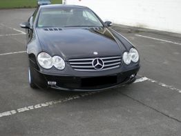 Schwarzer Mercedes-Benz auf Parkplatz mit weißen Markierungen, im Hintergrund grüne Wiese.