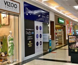 Corredor de shopping com lojas, manequins vestidos e placa de transferência de dinheiro.