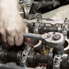 Hand using a wrench on an engine's camshaft assembly.