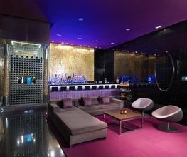 Bar moderno con sofá, sillas blancas y luces púrpuras. Decoración elegante y contemporánea.