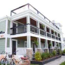 Two-story building with balconies and bikes outside, featuring greenery and large windows.