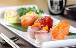 Vassoio di sushi colorato con pesce crudo e uova di pesce, accompagnato da bacchette giapponesi.