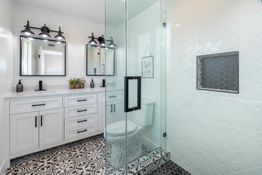 Modern bathroom with glass shower, white cabinets, dual mirrors, and patterned floor tiles.